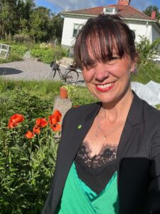 Cathrin Vinge står i sin trädgård och ler mot kameran.