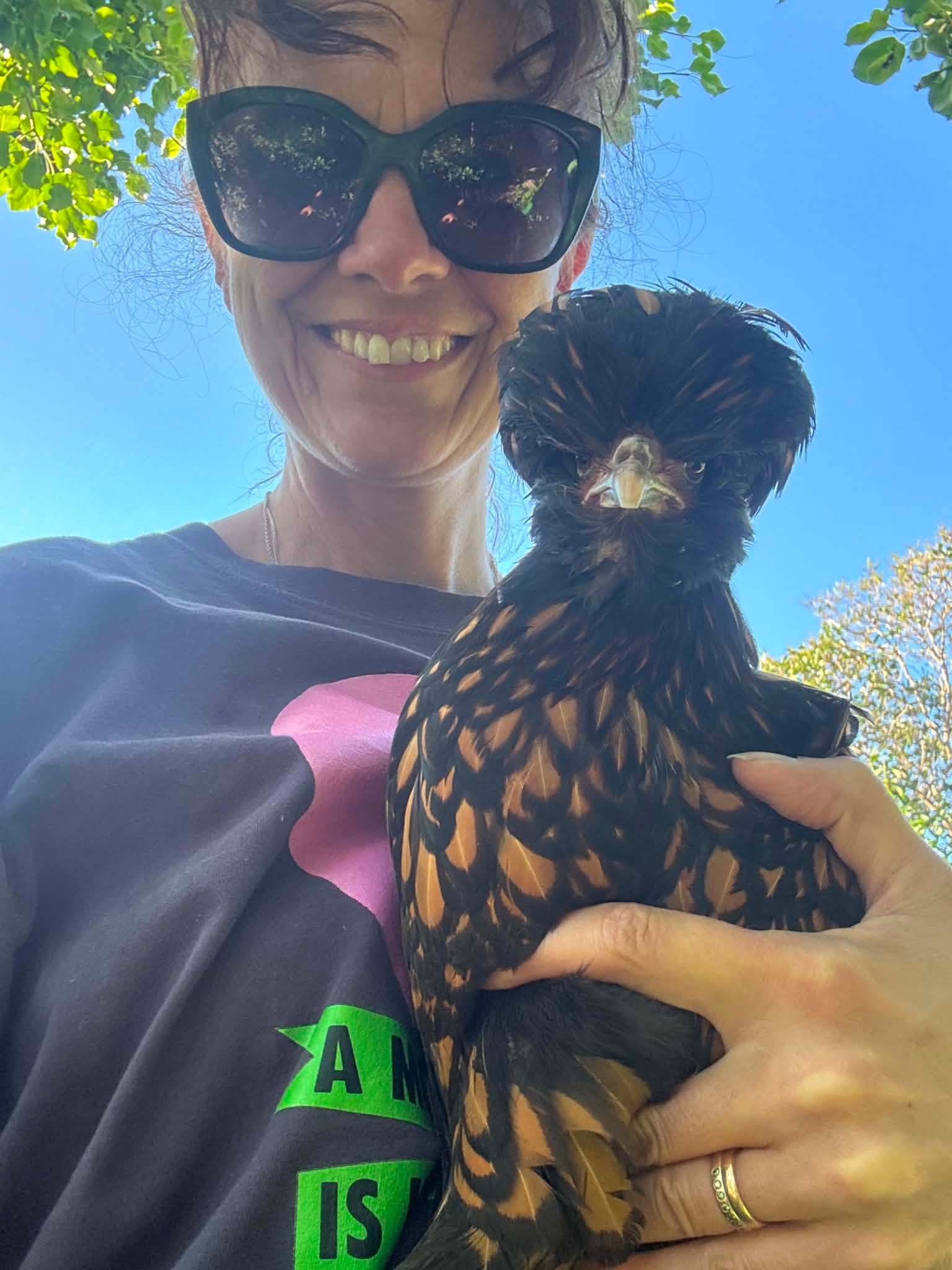 Cathrin tar en sommar-selfie med en av sina höns. En klarblå himmel syns bakom dem.